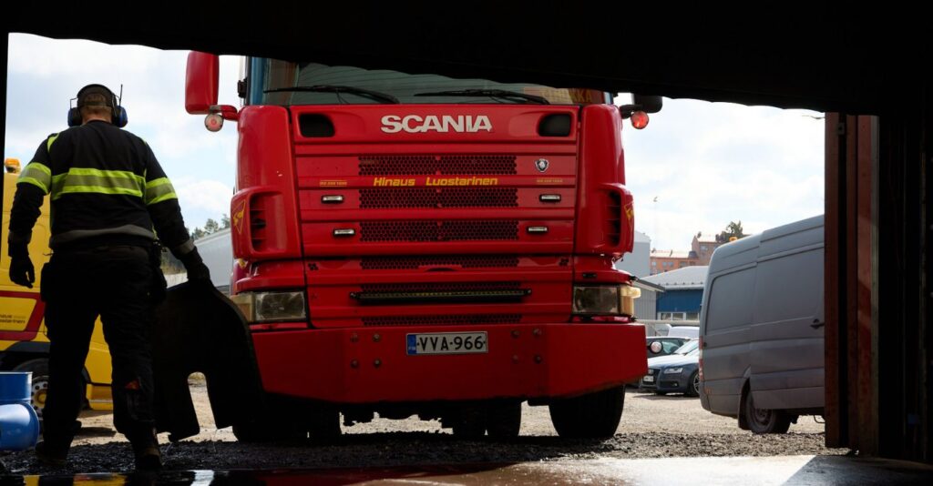 Scania-merkkinen punainen hinausauto, jonka vierellä harmaa pakettiauto ja hinausauton kuljettaja menossa kohti autoa